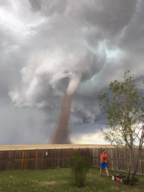 Man casually mowing the lawn with a tornado behind him. Says he was "keeping an eye on it."