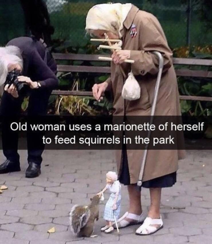 Old woman uses a marionette of herself to feed squirrels in the park.