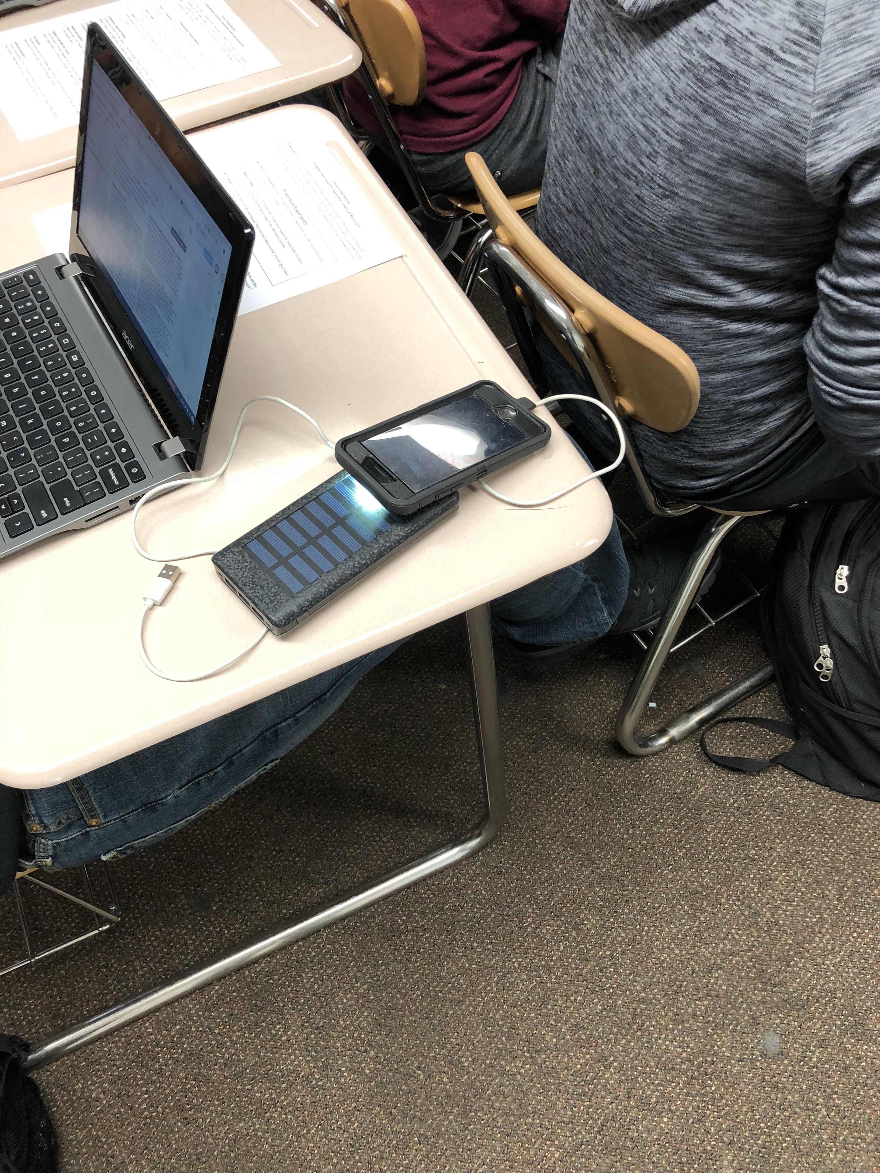 Student tries to charge solar panel external battery using the light from their phone so that they can charge their phone.