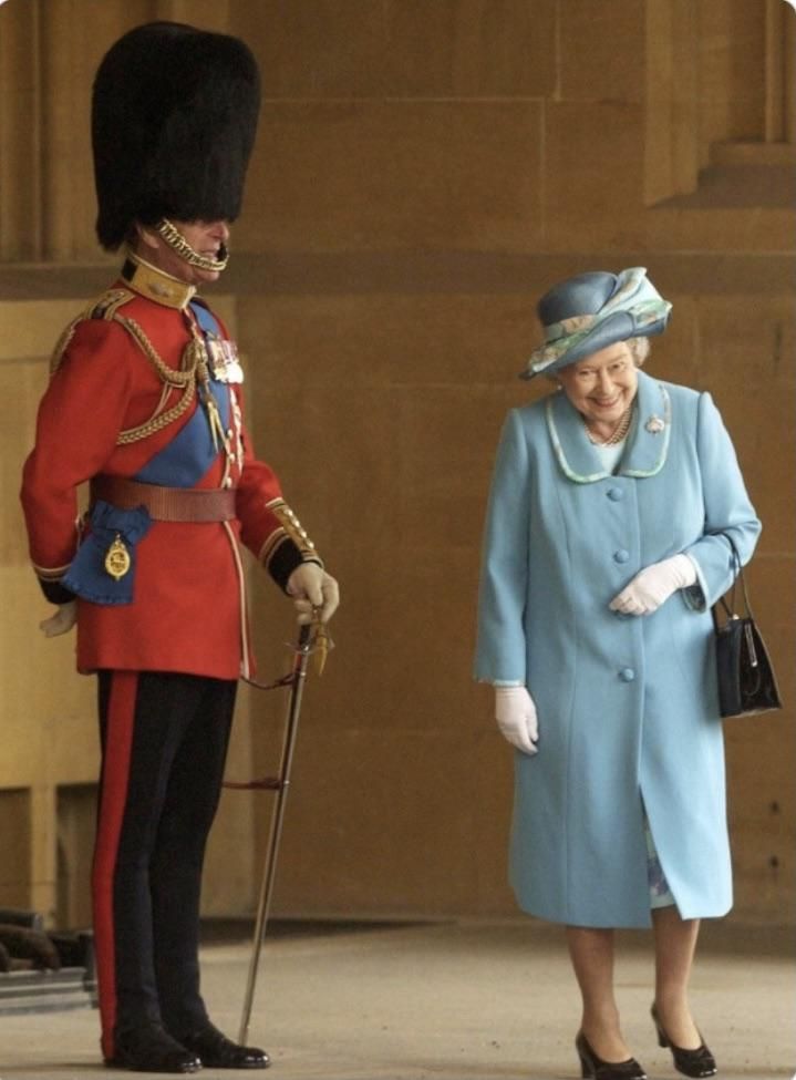 The queen trying not to laugh as she passes her husband in uniform.