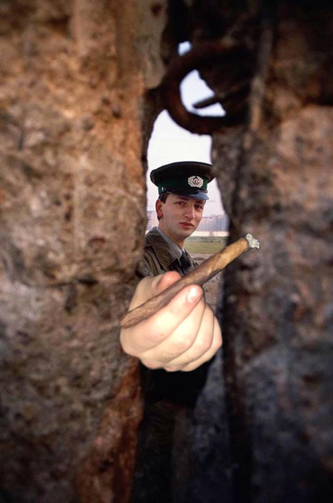 An East German border operative passes the boof trough a hole in the Berlin Wall.